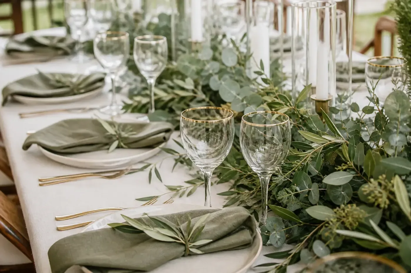 Mesa de recepción con camino de follaje, platos ivory y servilletas sage